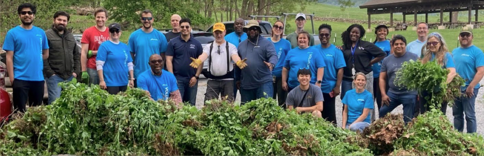 group of 23 volunteers posed with pile of invasive plants than have been pulled out