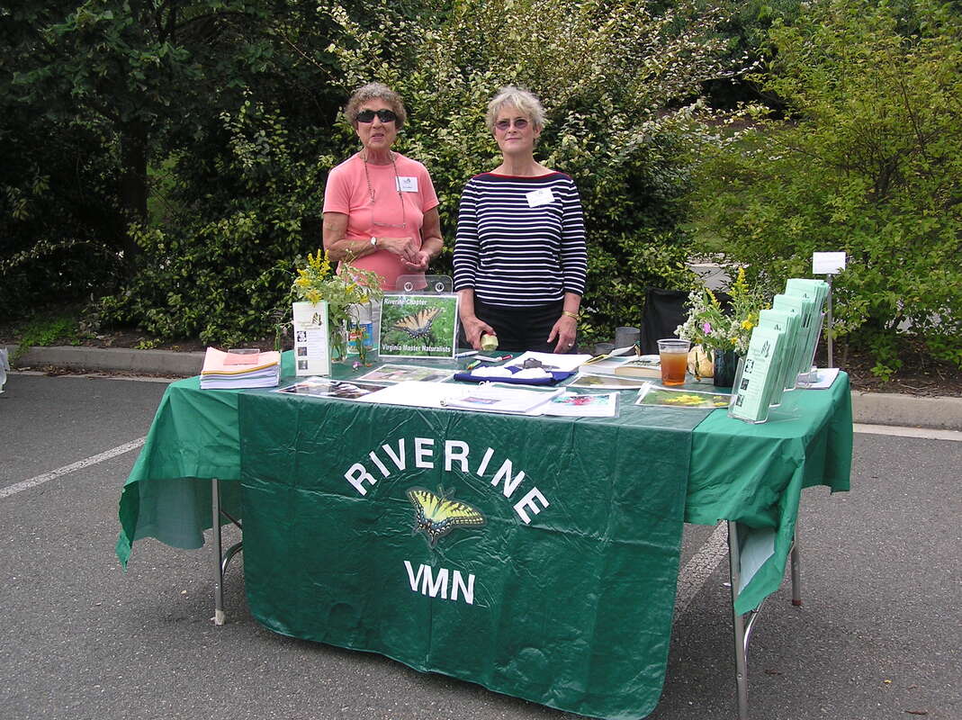 two volunteers at a display table with Riverine VMN banner