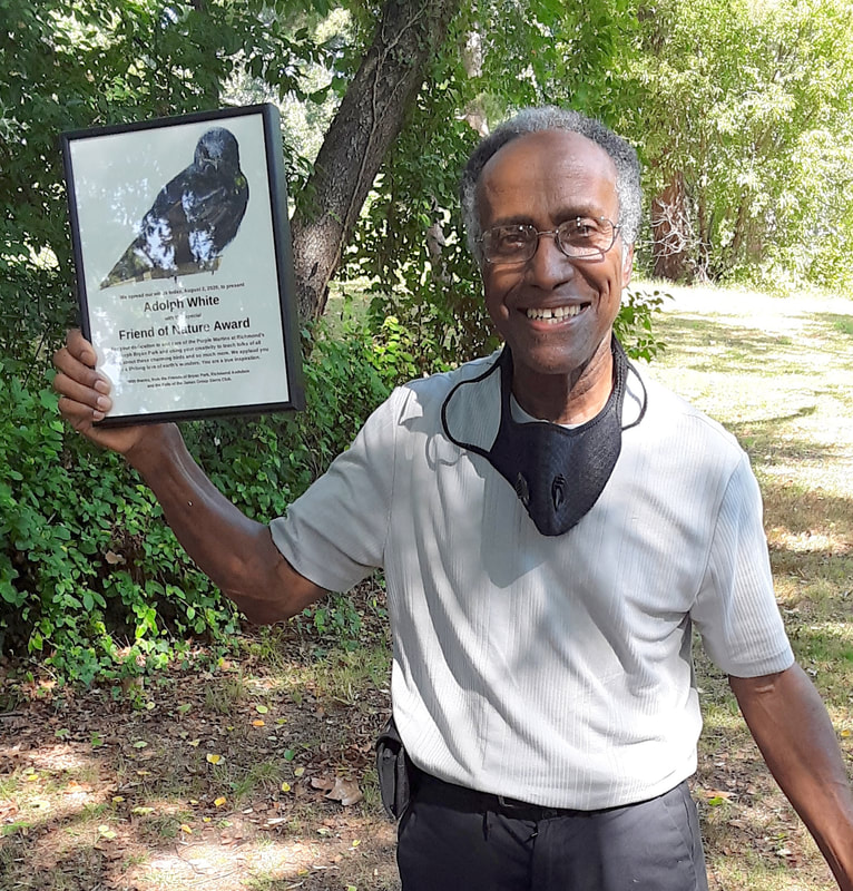 Photo of man outside in a park holding framed award with a picture of a purple martin bird on it