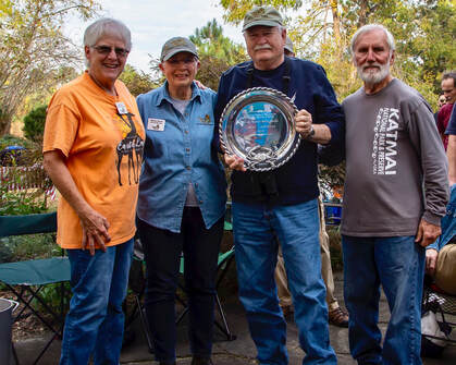 VMN volunteer Les Lawrence holding a large silver award platter with a crab on it, standing with three other volunteers outside.
