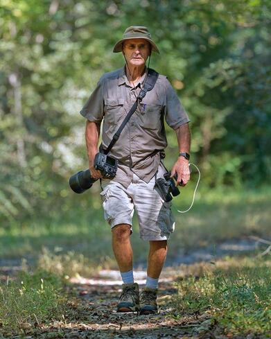 naturalist hiking on a trail with camera with telephoto lens and binoculars