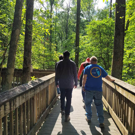 group of five people walking on a boardwalk through a forest