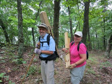 two volunteers carrying lumber on a trail in a forest