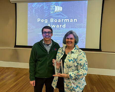 volunteer posed with a parks employee holding a glass award in front of a screen that says Peg Boardman Award