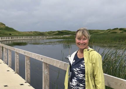 smiling volunteer posed on a boardwalk in a marshy area
