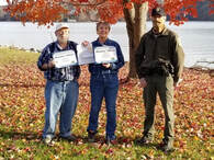 two people posed with certificates next to park ranger by a lake