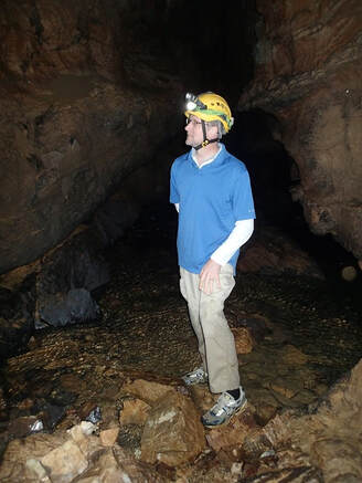 man wearing a helmet with a light, standing in a cave