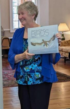 smiling volunteer holding up a book about birds