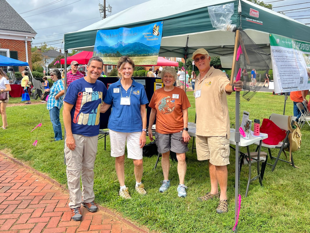 four volunteers posed in front of a popup tent with display table and Virginia Master Naturalist banner