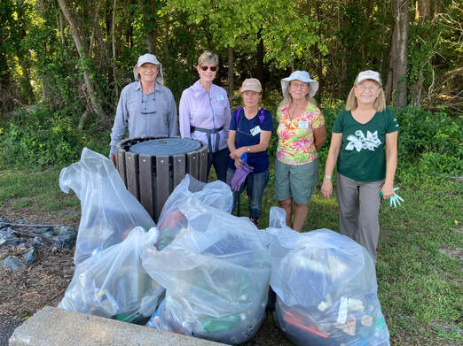 five volunteers on the edge of a wooded area with several very large bags of trash