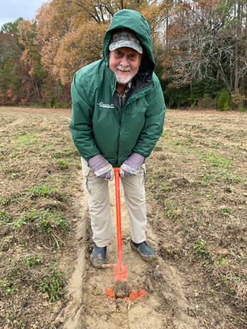 man using soil borer to prepare for planting a tree in a field