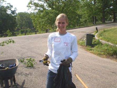 Woman holding garden clippers and trash bag, removing invasive plants at a park.