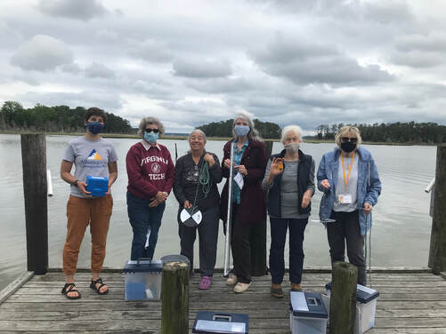 6 people on a dock by a waterway holding water monitoring equipment