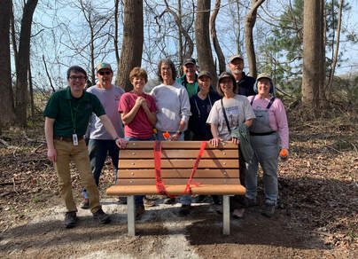 volunteers and park employee posed with a bench in a wooded area