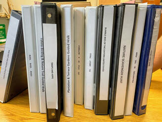 notebooks labeled with names of interpretive programs and lined up on a shelf