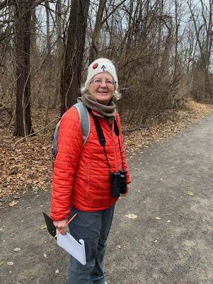 volunteer walking down a trail with a clipboard and binoculars