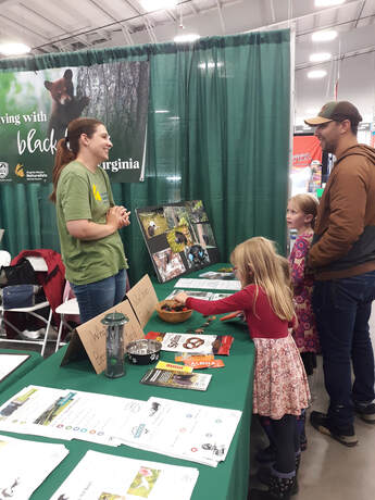 volunteer at a booth with items about black bears, talking to a man and two children
