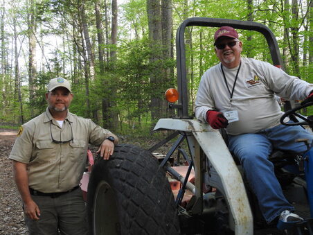 volunteer and ranger posed with heavy machinery in forest