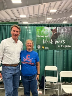 Governor posed with volunteer in front of banner that reads Living with Black Bears in Virginia