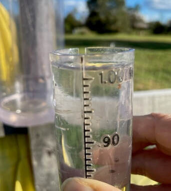 a person's hand holding a clear plastic cylinder with measurement markings on the side