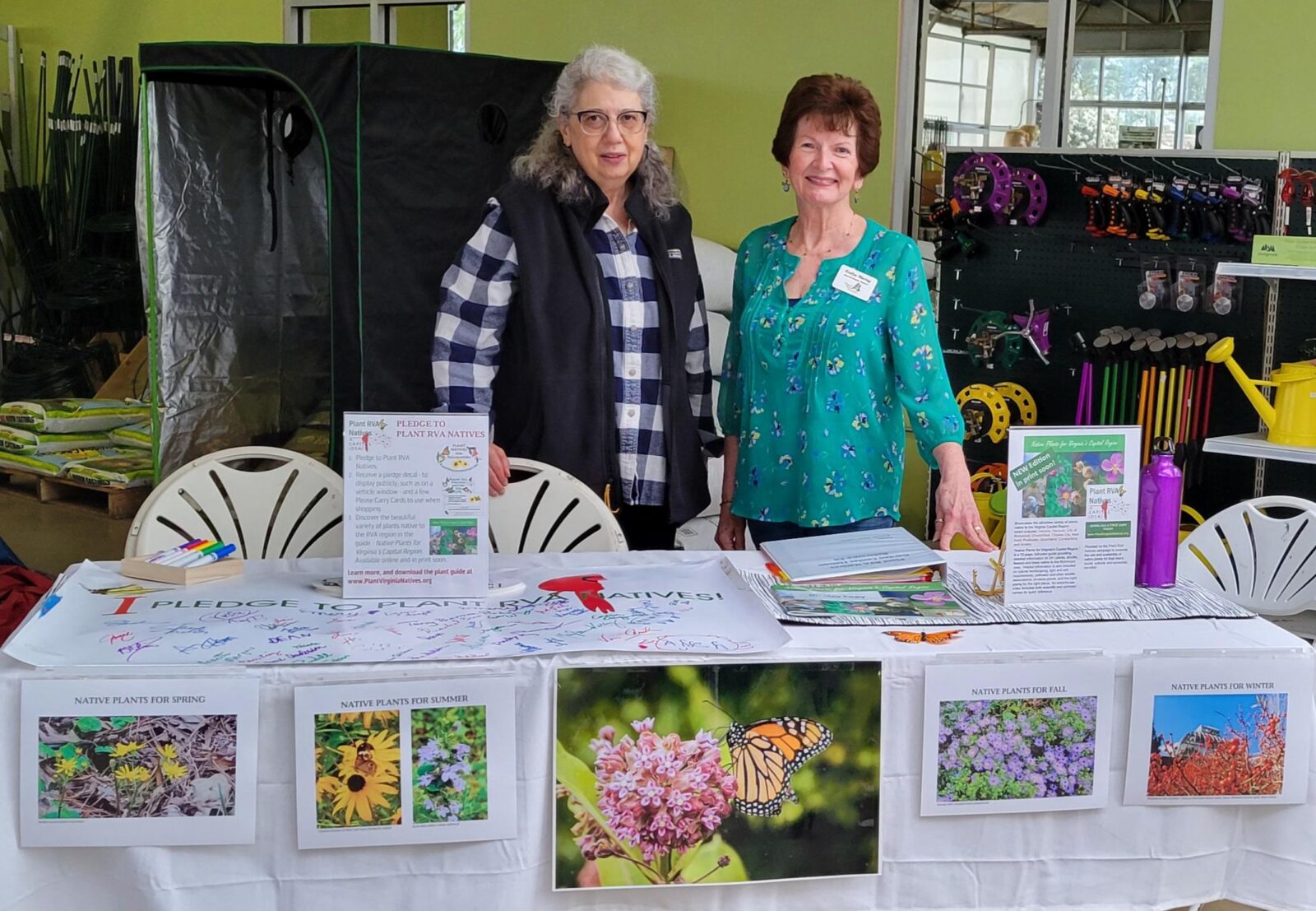 two volunteers posed at table with pictures and information about native plants