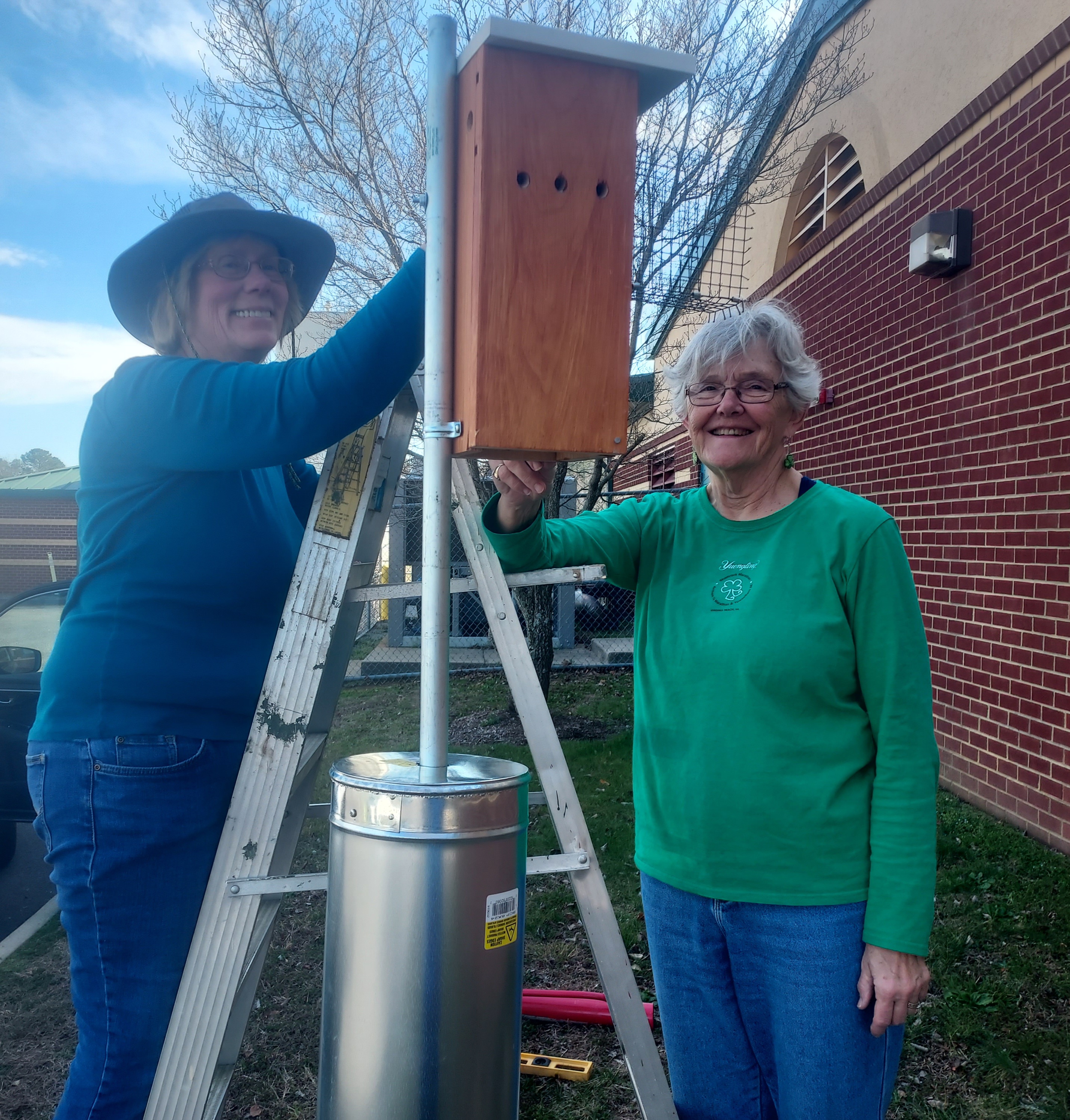 two volunteers putting up a bluebird nest box outside a school.