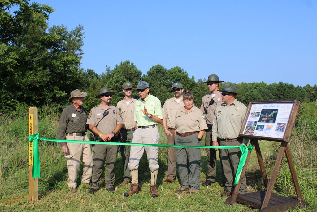 group of park rangers with two volunteers, about to cut a ribbon across a walking trail