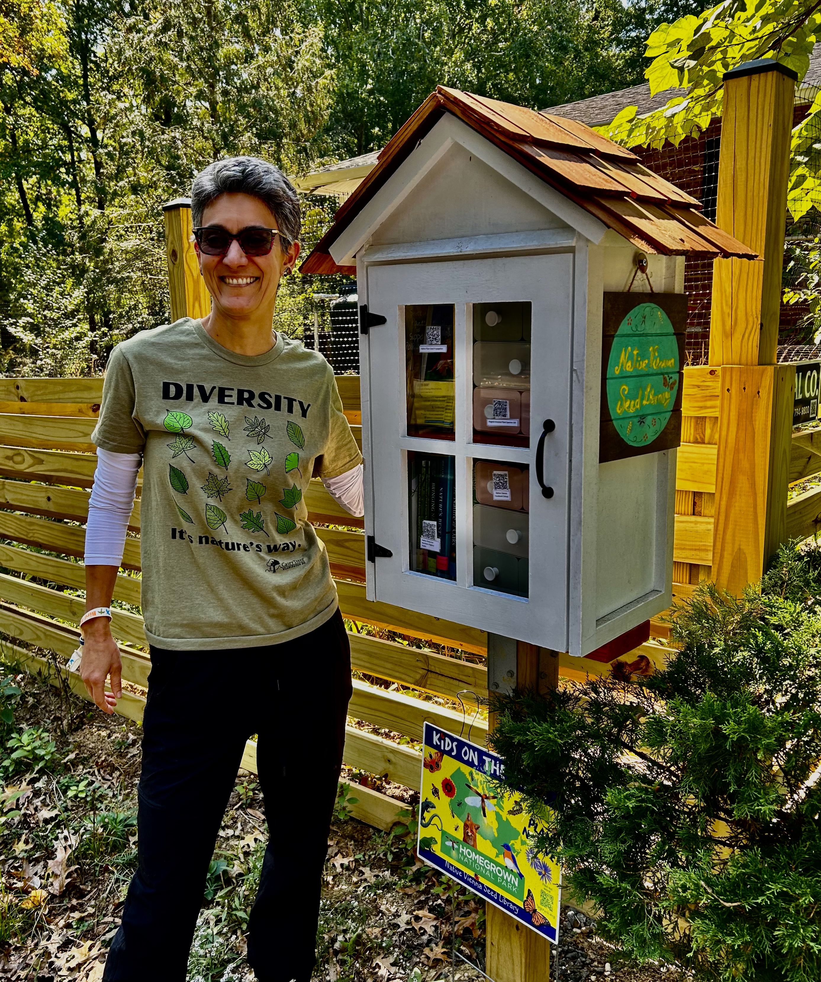 person posed next to a box on a post, containing books and seed packets