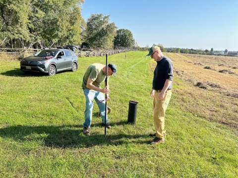 two volunteers installing a pole for a birdhouse in an open field