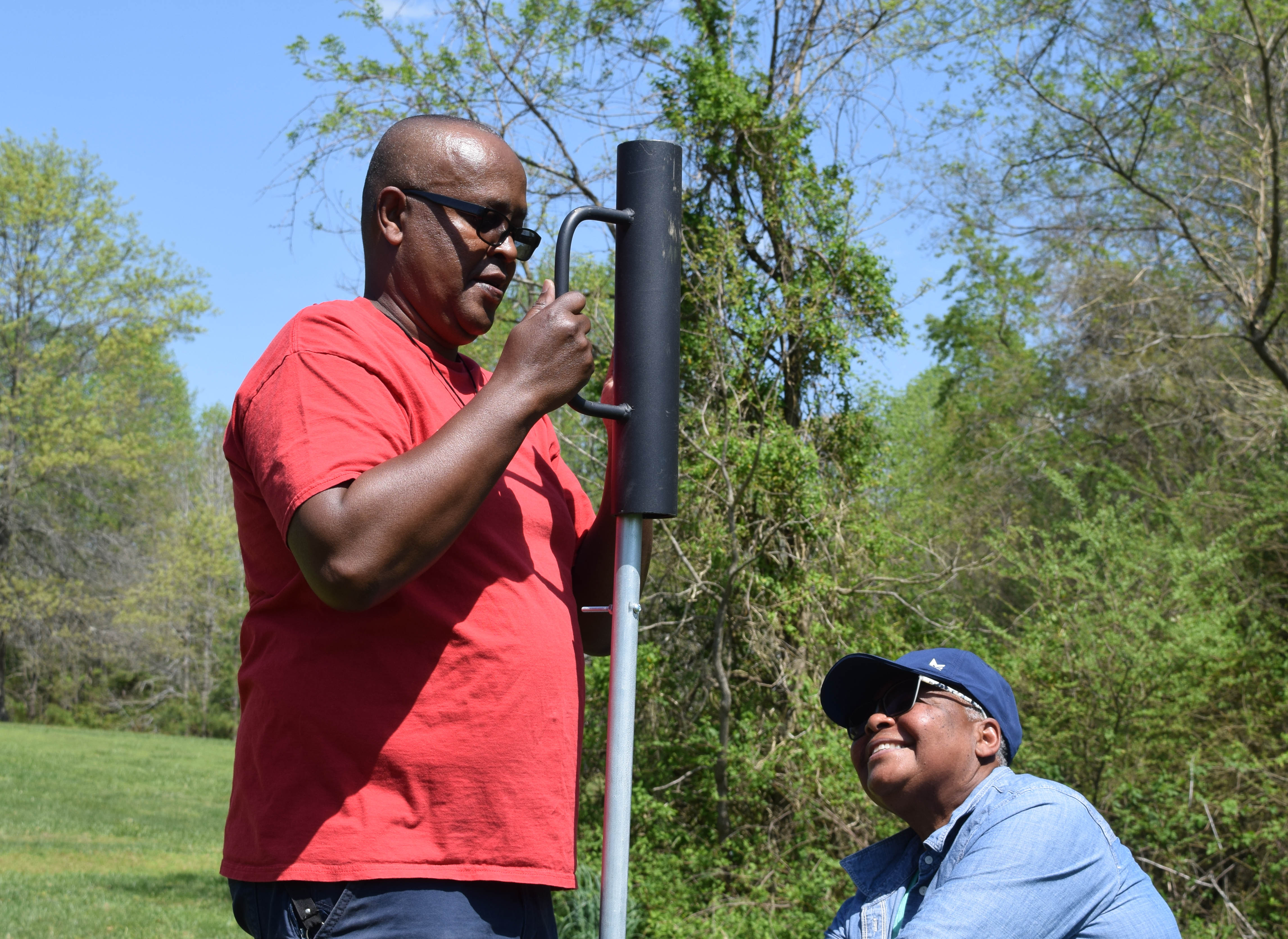 person using a post hole driver to put a metal pole in the ground