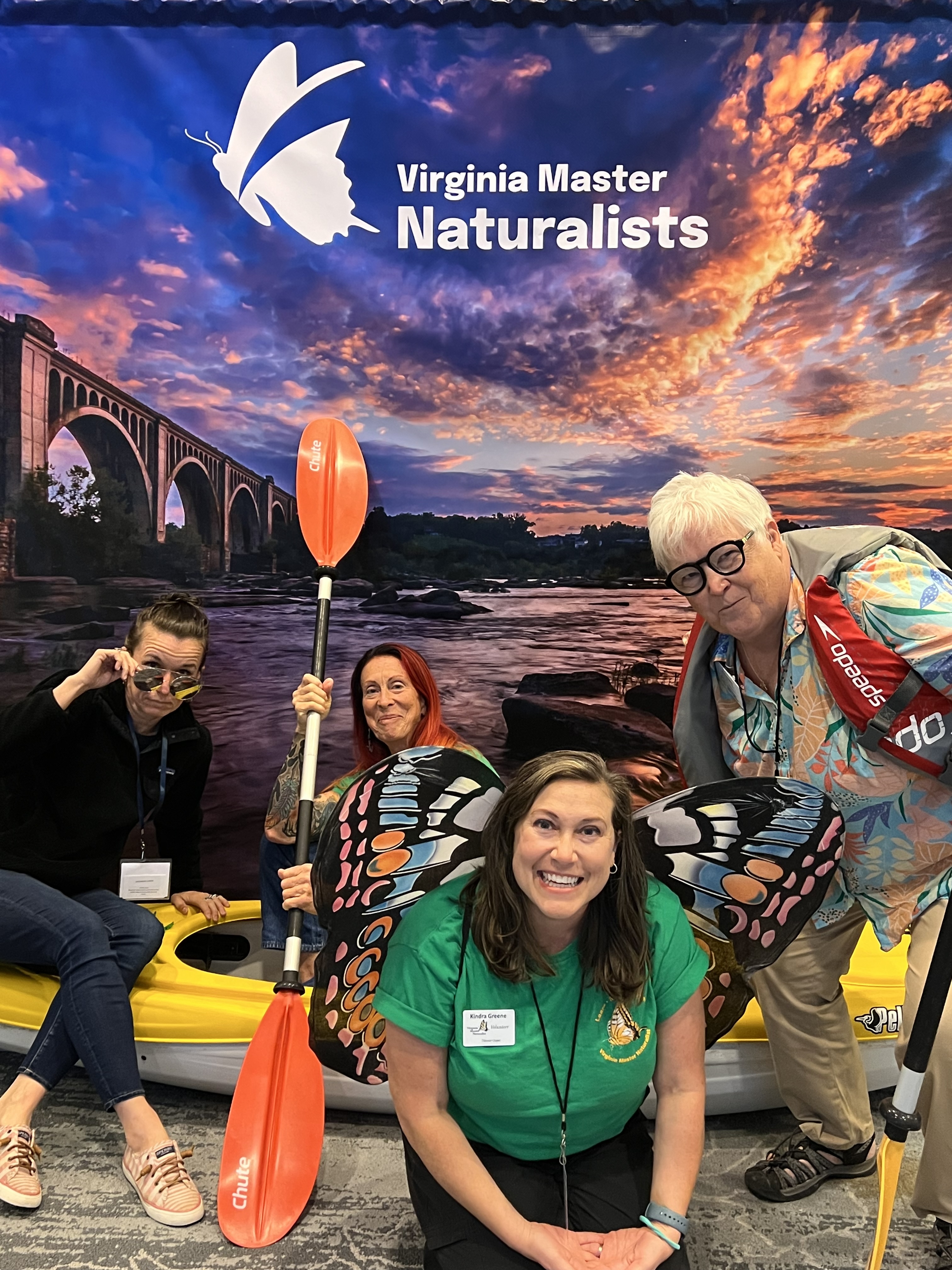four people posed with paddles and a kayak in front of a photo backdrop showing a river scene