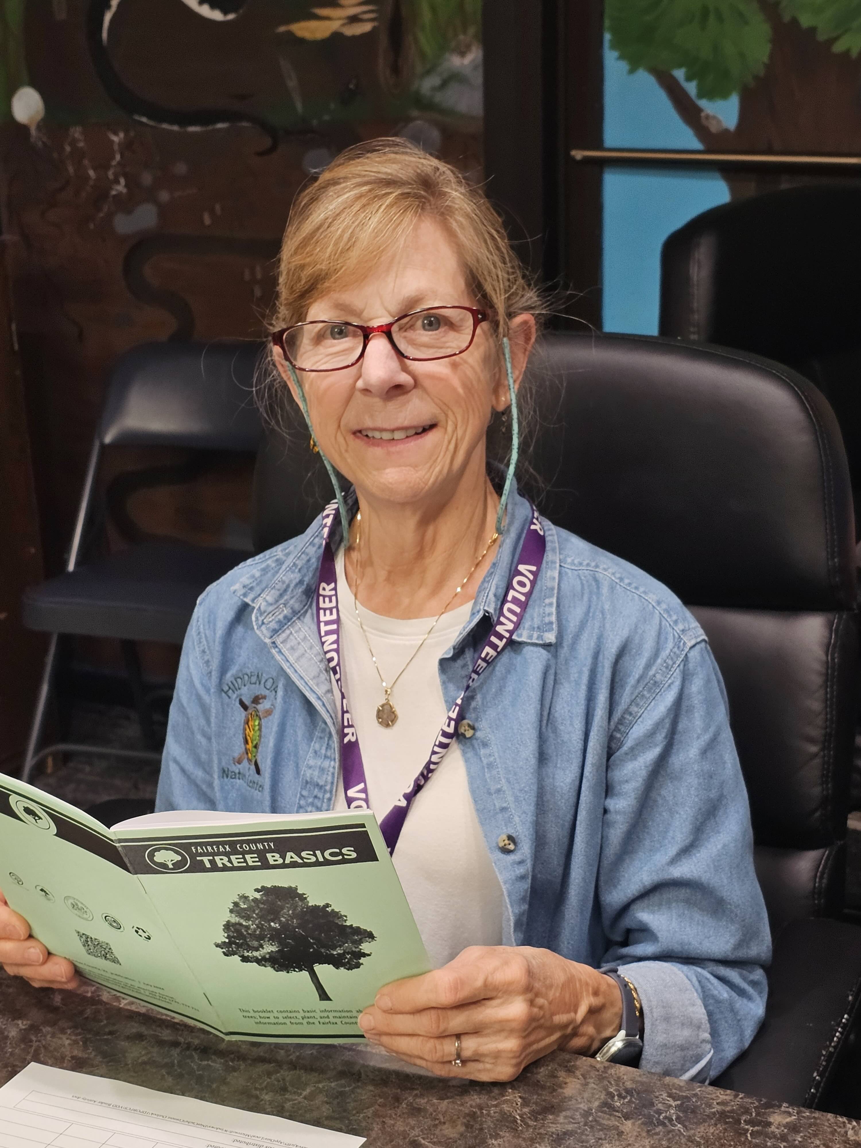 Woman at a desk, looking up from a Fairfax County Tree Basics publication