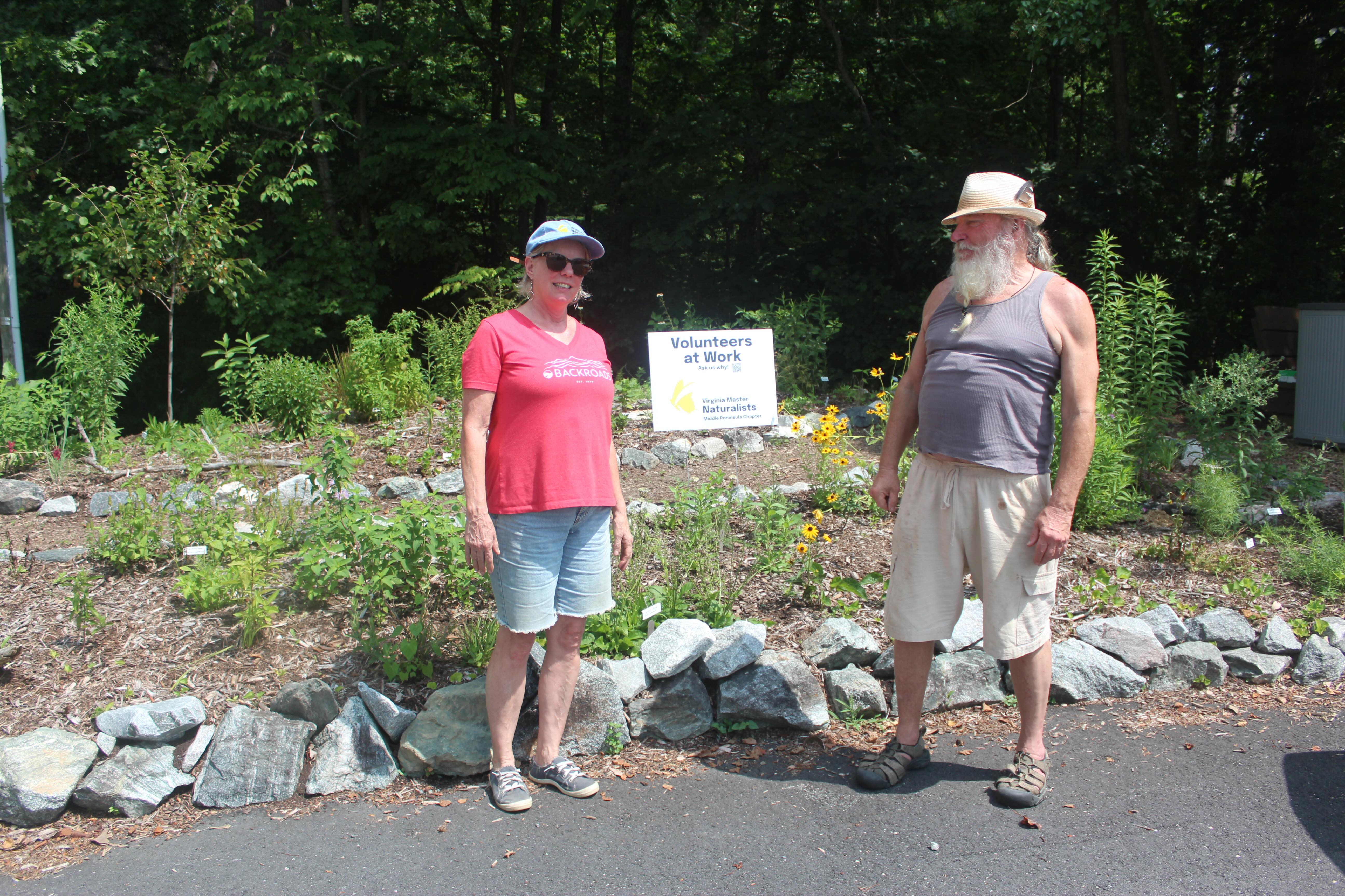 two volunteers posed in front of a garden with a sign reading Virginia Master Naturalist Volunteers at Work