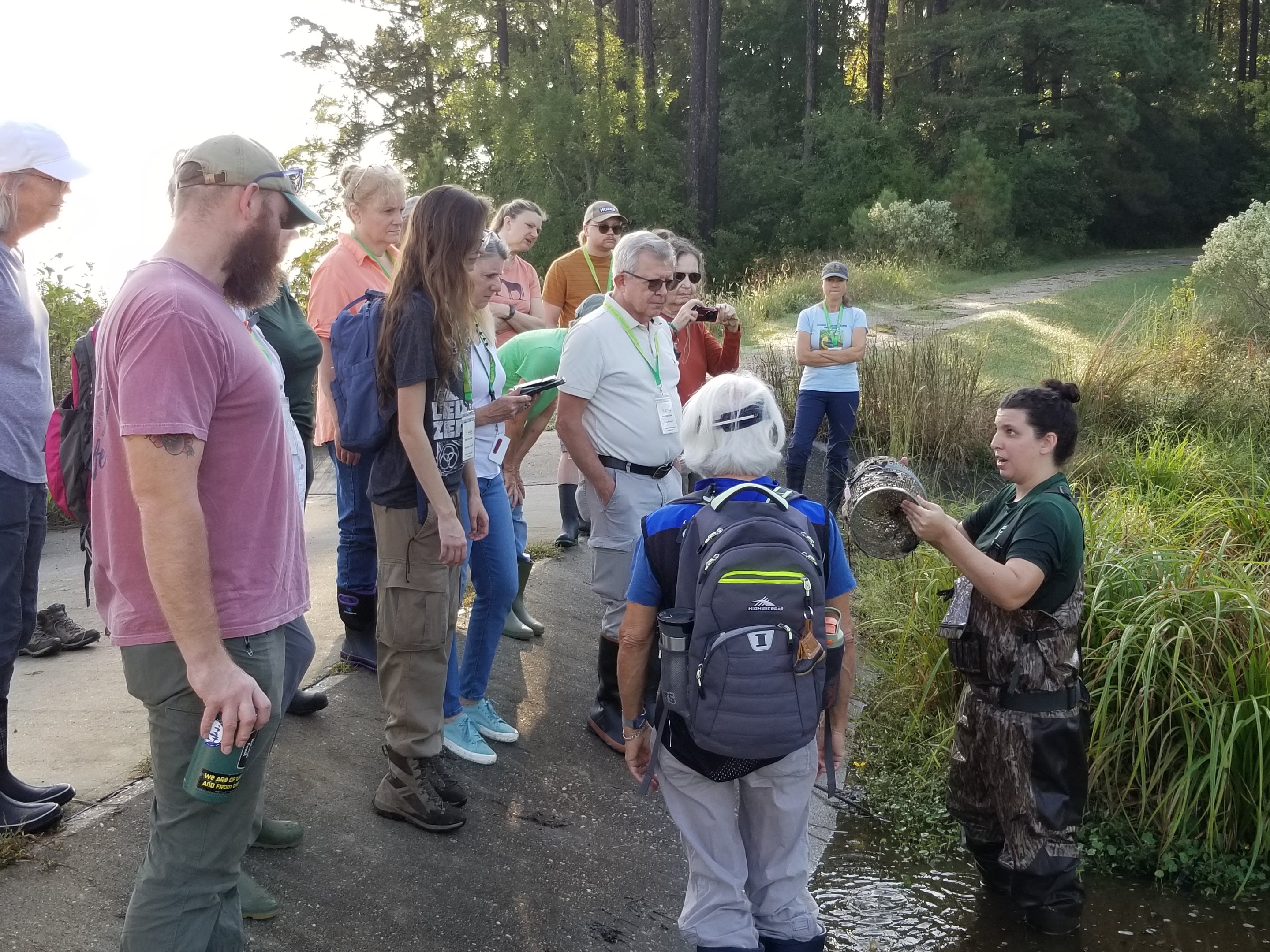 wildlife biologist in water, wearing waders, showing a turtle trap to a group of people