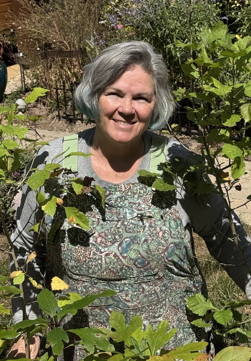 smiling woman in overalls posed in the midst of green shrubs