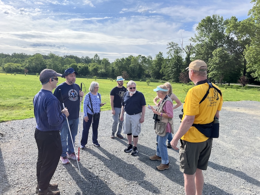 group of people standing on a gravel road. Two people have white canes as would be used by people with vision impairment