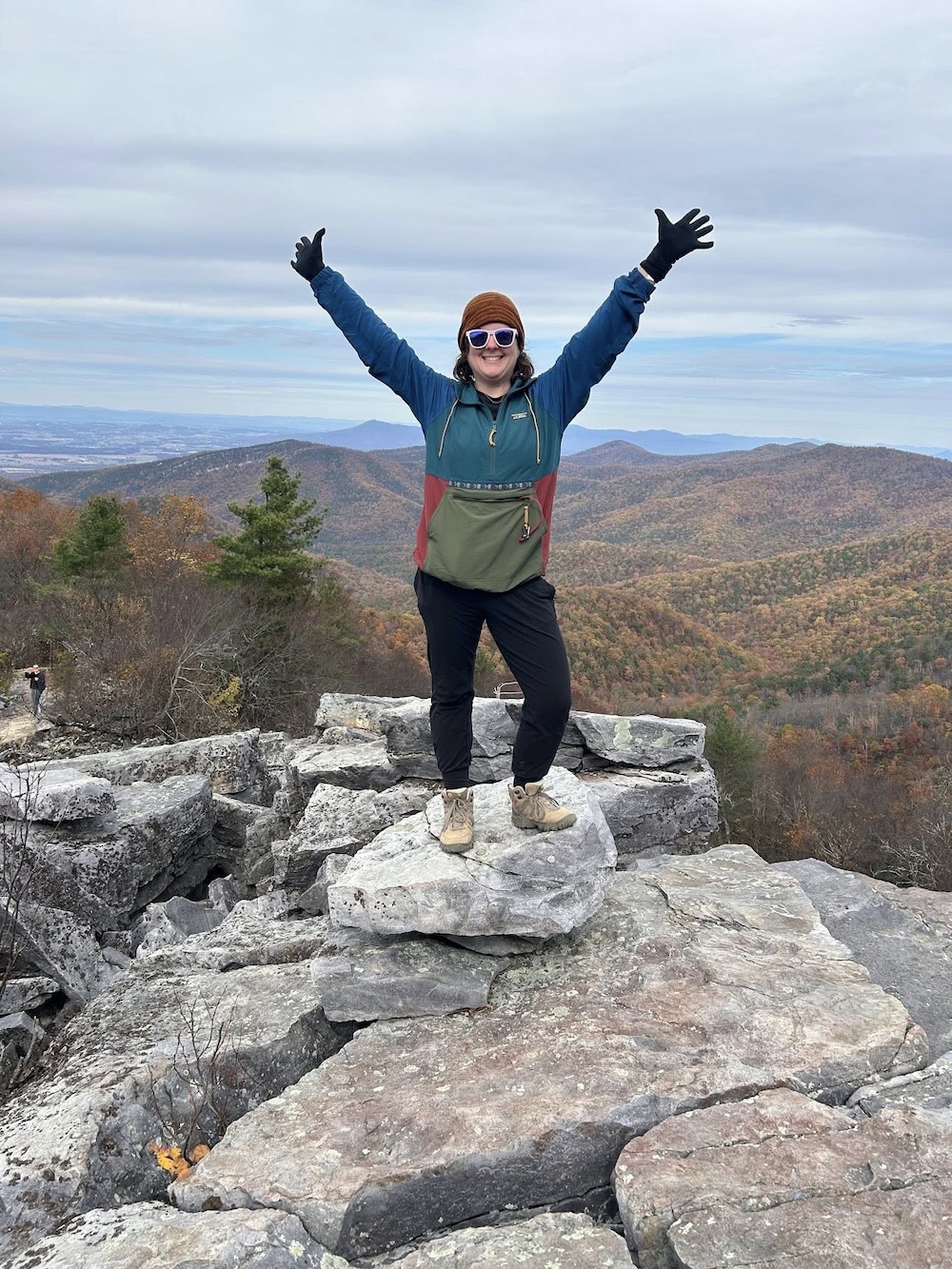 A person standing on a rocky outcrop with her arms in the air