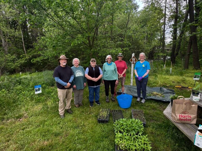 six volunteers posed outdoors with flats of native plants and gardening tools