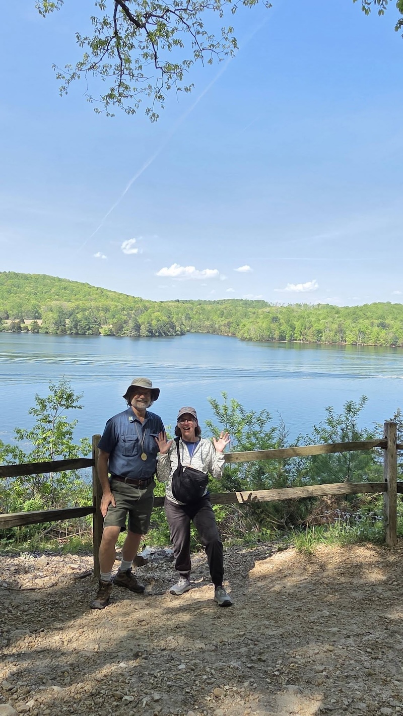 two people posed by a fence next to a lake