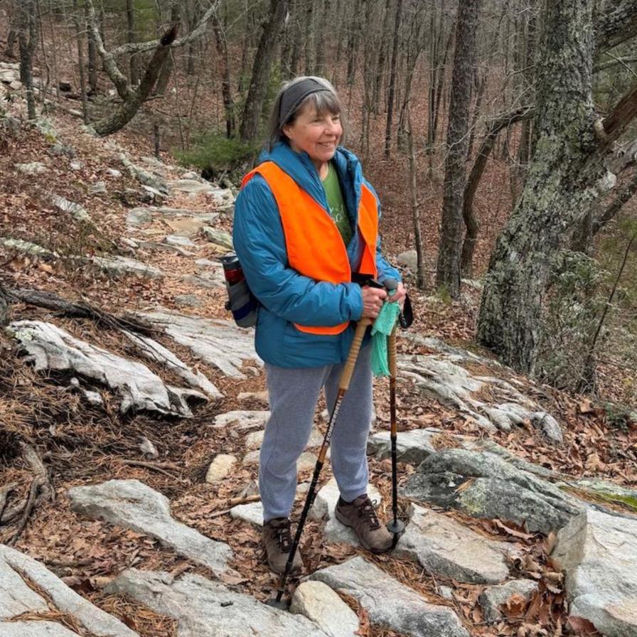 Volunteer in blaze orange vest, holding hiking poles, posed on a rocky outcrop