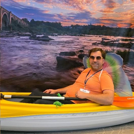 Kevin Divins posed in a kayak in front of a backdrop with a river scene